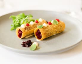Zwei knusprige, goldbraune Cannoli-ähnliche Röhren gefüllt mit einer reichhaltigen, dunklen Beerenkompott, garniert mit cremiger Sauce und frischen jungen Kräutern, serviert mit einem Klecks Beerenmarmelade.