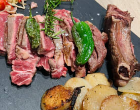 Carne asada de res y chuletas de cordero, acompañadas de papas asadas y verduras salteadas.