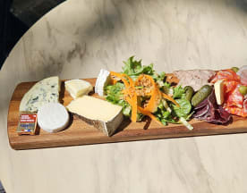 Planche de charcuterie élégamment présentée avec une variété de fromages, de viandes séchées, une salade fraîche, des cornichons et des olives.