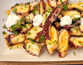 Pulpo a la parrilla con salsa cítrica, adornado con hierbas frescas y pequeñas porciones de salsa cremosa.