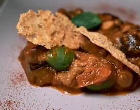 Plato rico con trozos tiernos de carne y pimientos verdes en una salsa espesa y sabrosa, decorado con crujientes y hojas de albahaca fresca.