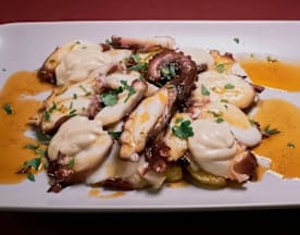 Pulpo a la parrilla con salsa cremosa, acompañado de rodajas de papa y hierbas frescas.