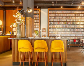 Interior de restaurante moderno con bar estilizado, taburetes amarillos y decoración ecléctica.