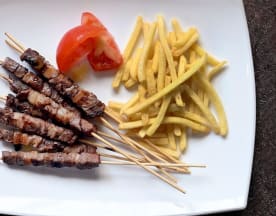 Spiedini di carne grigliata con patatine fritte croccanti e pomodoro fresco.