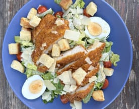 Salade fraîche avec des morceaux de poulet panés croustillants sur un lit de laitue romaine, garnie de tomates cerises, de croûtons croquants, d'œufs durs et de copeaux de parmesan.