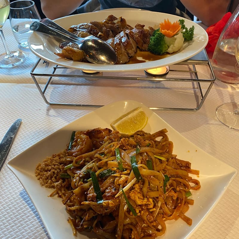 Sélection de plats avec un canard rôti, servi sur un lit de chou finement émincé, accompagné de sauces pour tremper, de wrappers de riz translucides, de concombre et d'oignons verts, ainsi qu'un bol de soupe.