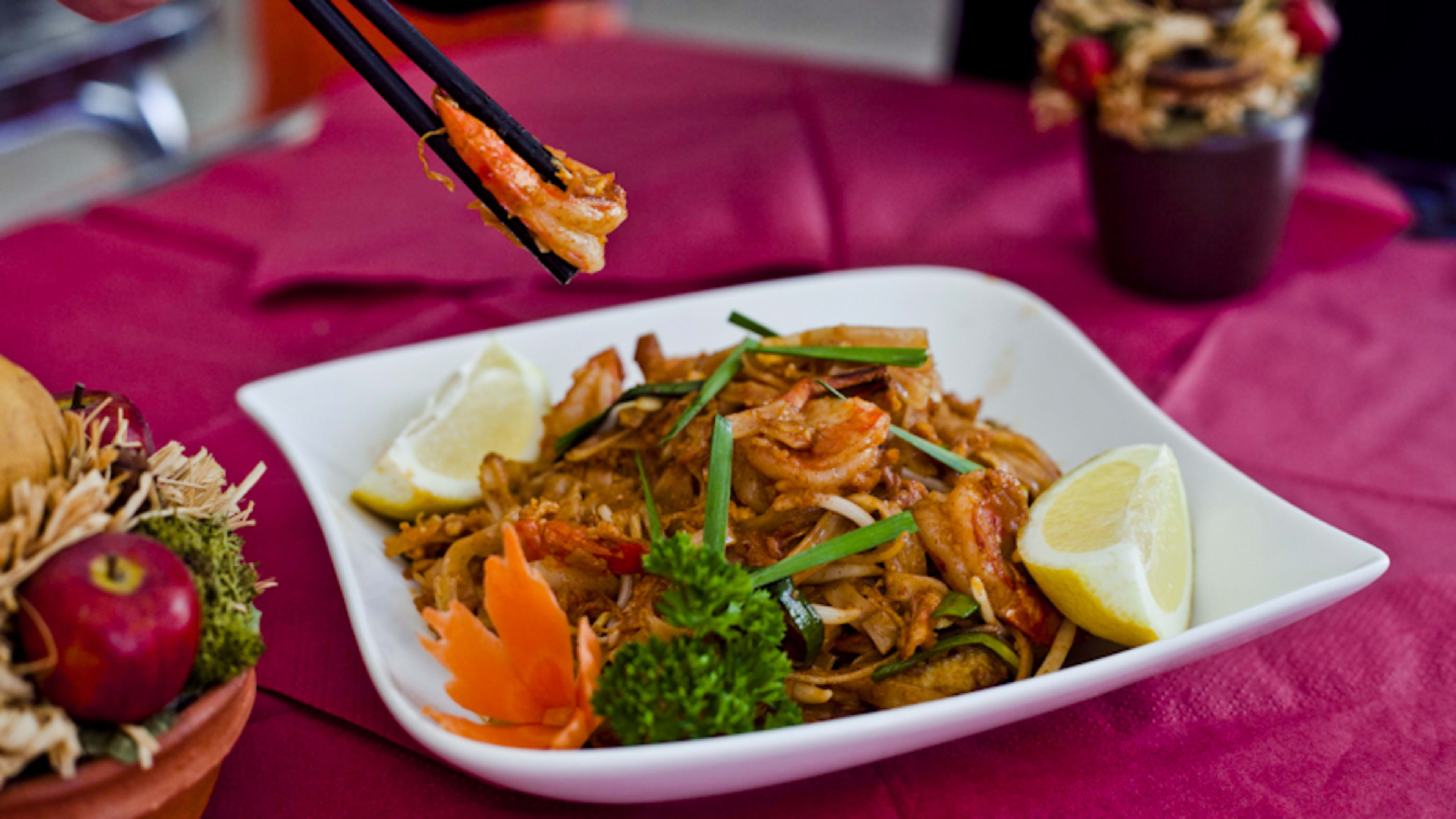 Plat généreux de nouilles sautées avec des crevettes et un mélange de légumes colorés, accompagné de quartiers de citron.