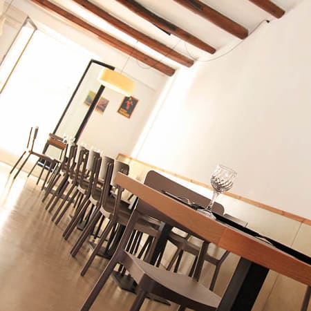 Interior de restaurante moderno con vigas de madera, suelo pulido, mesas de madera simples y sillas minimalistas, creando un ambiente acogedor y contemporáneo.