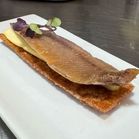 Pescado ahumado o curado sobre una base crujiente, acompañado de una capa cremosa y decorado con microgreens.