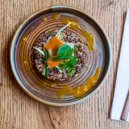 Plat de quinoa coloré, garni de carottes finement tranchées et d'herbes fraîches, accompagné d'une sauce orange vive au goût citronné.