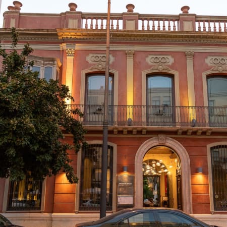 Exterior de un restaurante histórico con detalles arquitectónicos elegantes, fachada en tono durazno, grandes ventanas con hierro forjado y un ambiente acogedor.
