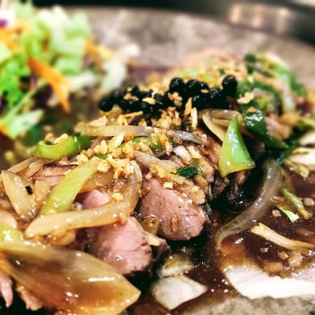 Tranches de viande tendre, probablement de bœuf, nappées d'une sauce savoureuse, accompagnées d'oignons sautés, d'une salade fraîche de légumes mélangés et de brocoli vapeur.