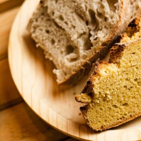 Fatias de pão rústico, uma de textura leve e macia, e outra densa e húmida, evidenciando um aspeto caseiro e artesanal.