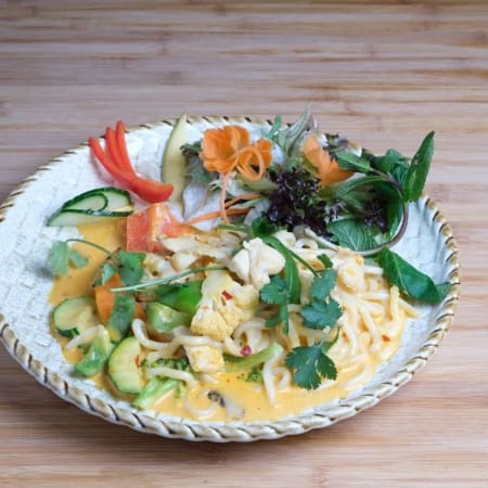 Pasta in einer cremigen, orangefarbenen Sauce, serviert mit frischen Gemüsewürfeln, darunter Gurken und Paprika, sowie Kräutern, Karotten und Blattsalat für zusätzliche Farbe und Textur.