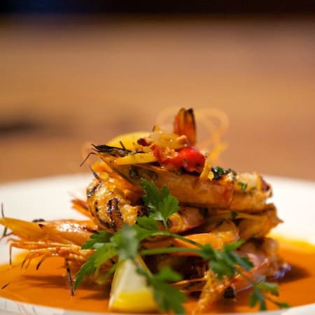 Succulent shrimp stacked high, chargrilled to a golden finish, served with a rich, spiced reddish-orange sauce and garnished with fresh cilantro and a lemon wedge.