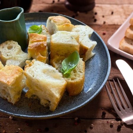 Freshly baked rustic bread with a golden crust and soft interior, served with a dipping sauce and garnished with basil leaves.
