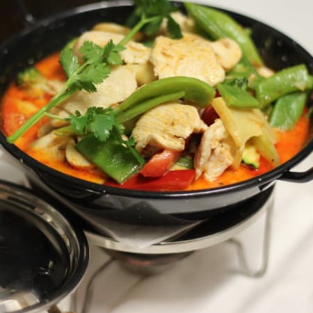 Zartes Hähnchen in einer aromatischen, leicht scharfen Sauce, umgeben von buntem Gemüse wie roten Paprika, knackigen Zuckerschoten und frischen Kräutern.
