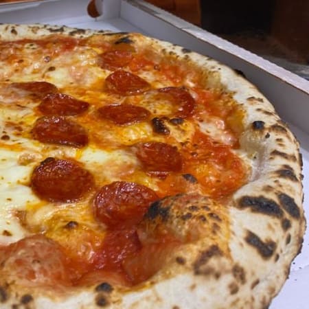 Pizza appena sfornata con crosta dorata e leggermente bruciacchiata, con salsa di pomodoro, mozzarella fusa, fette di pepperoni croccanti e foglie di basilico fresco.