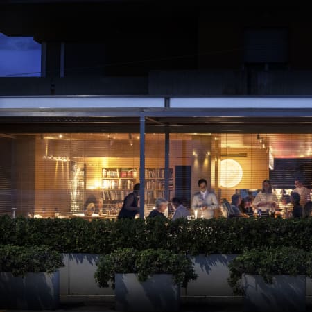 Esterno di un ristorante moderno con illuminazione calda, piante verdi e un'atmosfera vivace.