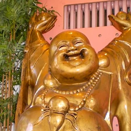Statue dorée d'un Bouddha rieur avec un ventre rond et une expression joyeuse, entourée de bambous verts, créant une ambiance accueillante et joyeuse.