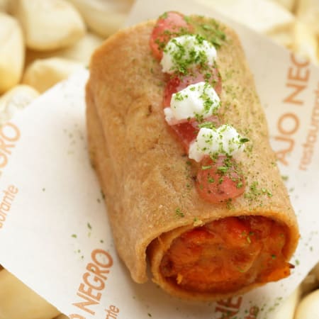 Tortilla crujiente rellena de carne y verduras, con salsa cremosa y hierbas frescas, acompañada de tomate picado.
