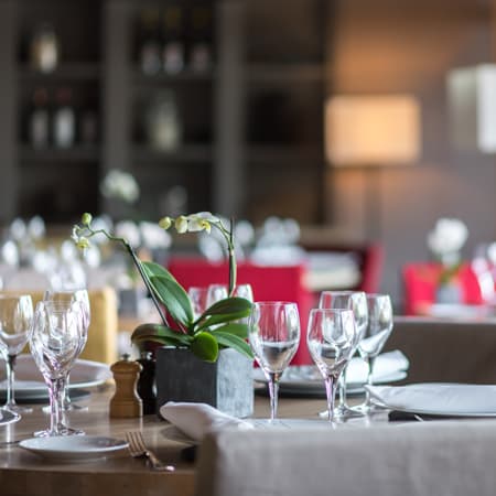 Intérieur de restaurant chaleureux et accueillant, avec des tables élégamment dressées, une orchidée en pot et un éclairage doux, créant une ambiance à la fois confortable et sophistiquée.