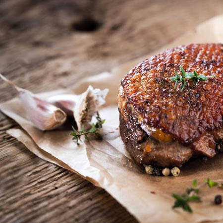 Perfekt gebratenes Fleisch, wahrscheinlich Ente oder Schwein, mit knuspriger, goldbrauner Haut und saftigem, zartem Fleisch, garniert mit frischem Rosmarin, Thymian und leicht gerösteten Knoblauchzehen.