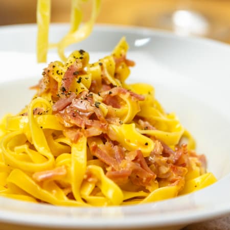 Fettuccine cremoso com pancetta crocante, coberto com um molho rico de ovo e queijo, guarnecido com pimenta preta e salsa.