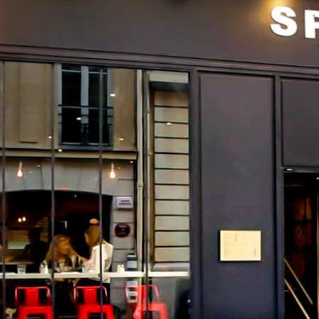 L'extérieur du restaurant moderne "Spezia Piadina & Co." présente un design sombre et élégant avec de grandes fenêtres en verre, tandis que l'intérieur offre une ambiance accueillante avec un éclairage chaleureux et une décoration contemporaine.
