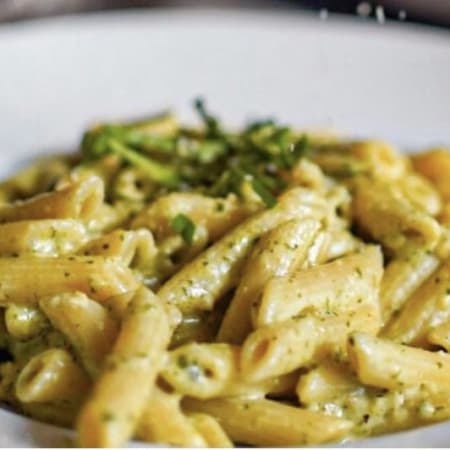 Plat de pâtes crémeux avec des penne enrobées d'une sauce pesto lisse, parsemées de basilic frais et d'herbes finement hachées pour une touche de fraîcheur.