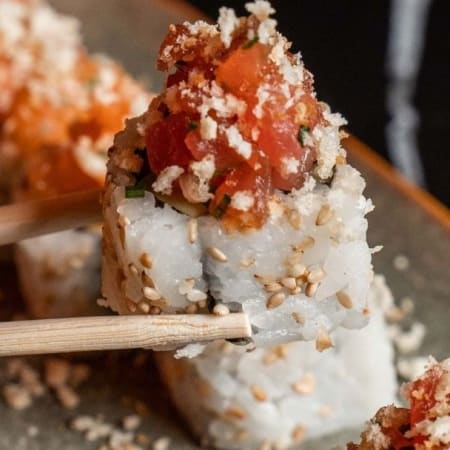 Sélection de rouleaux de sushi garnis de tomates finement hachées et de noix concassées, probablement du sésame, offrant une expérience fraîche et savoureuse.
