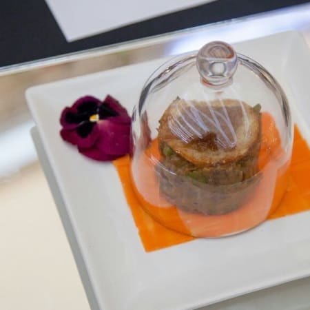Carne tierna con una suave salsa naranja y una flor comestible, presentada de manera artística.