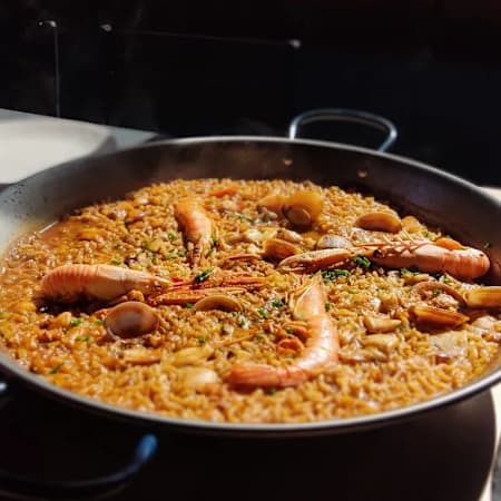 Paella con arroz al azafrán, mariscos como camarones y mejillones, y decorada con hierbas frescas.