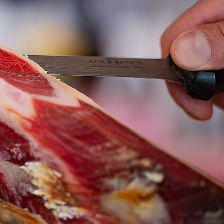 Jamón curado con vetas de carne roja y rosa, acompañado de una textura tierna y un exterior rústico que refleja su proceso de curación tradicional.