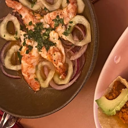 Tres tacos de frijoles o lentejas con aguacate, acompañados de camarones a la parrilla sobre cebolla y pimientos.