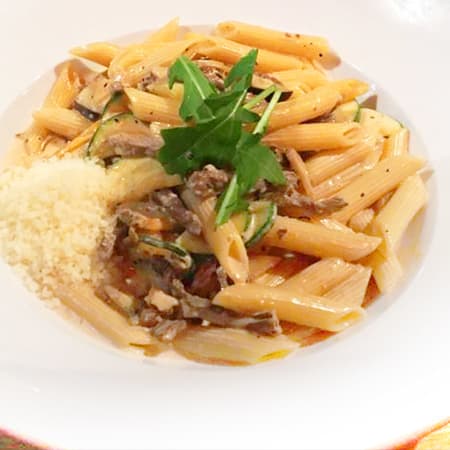 Pennepasta kokt al dente, blandad med en rik sås, mört kött och stekta grönsaker, garnerad med färska örter och riven ost.