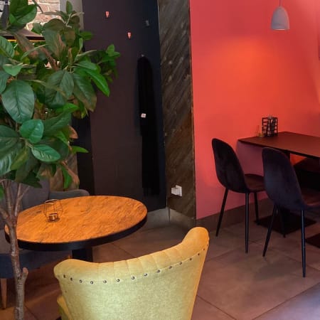 Intérieur de restaurant chaleureux avec des murs roses doux, des étagères en bois foncé, des chaises noires modernes et une table en marbre, créant une ambiance accueillante et stylée pour un repas décontracté.
