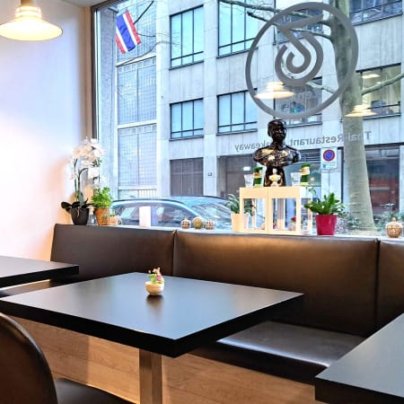 Intérieur de restaurant cosy au design minimaliste, avec des tables noires et des chaises sombres, éclairé par une grande fenêtre et décoré d'œuvres d'art subtiles.