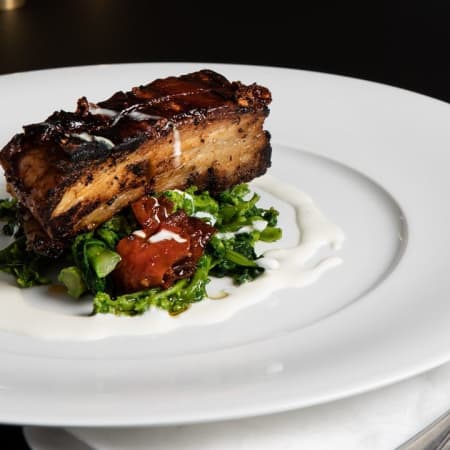 Pancetta caramellata con salsa cremosa, servita su un letto di verdure saltate e pomodori arrosto.