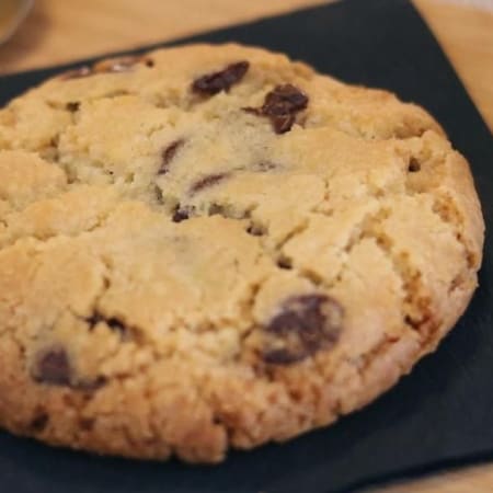 Grote, goudbruin koek met een krokante rand en een zachte, taaie binnenkant, bezaaid met gesmolten semi-zoete chocoladeschilfers voor een glanzende uitstraling.