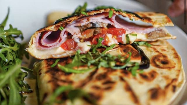 Pain plat grillé garni de jambon, fromage fondu et tomates en dés, accompagné de roquette fraîche.