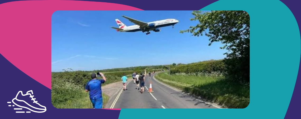 Photo of a plane low in the sky flying over a road lined with runners