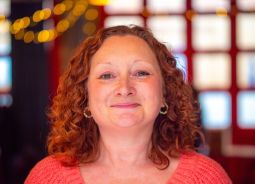 A white woman with curly red hair and a bright red top smiles directly at the camera