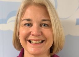 a white lady with a short blonde bob and a red polo shirt smiles broadly at the camera