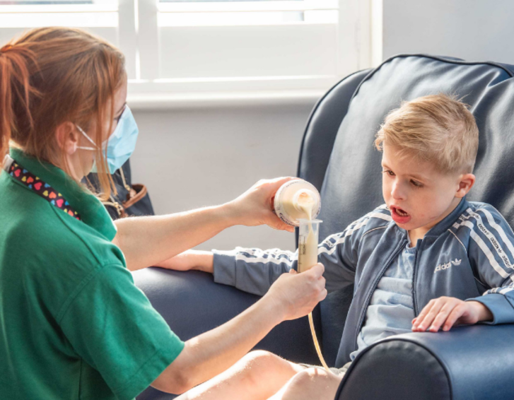 Nurse giving tube feed to young boy at a children's hospice