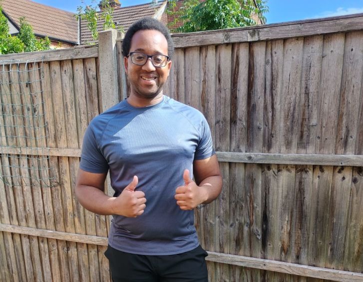A man is smiling at the camera with his thumbs up. He is wearing running kit and stood in his garden.