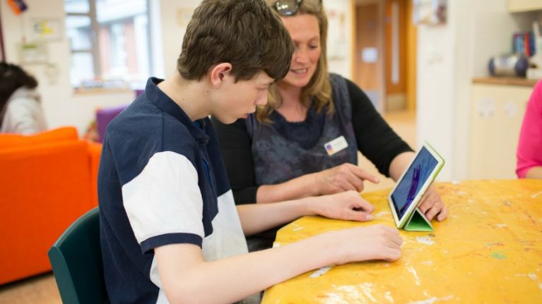 Teenage boy with carer looking at computer tablet