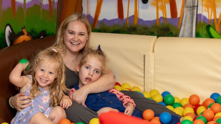 A mother and her two daughters sitting in a soft play ball pit