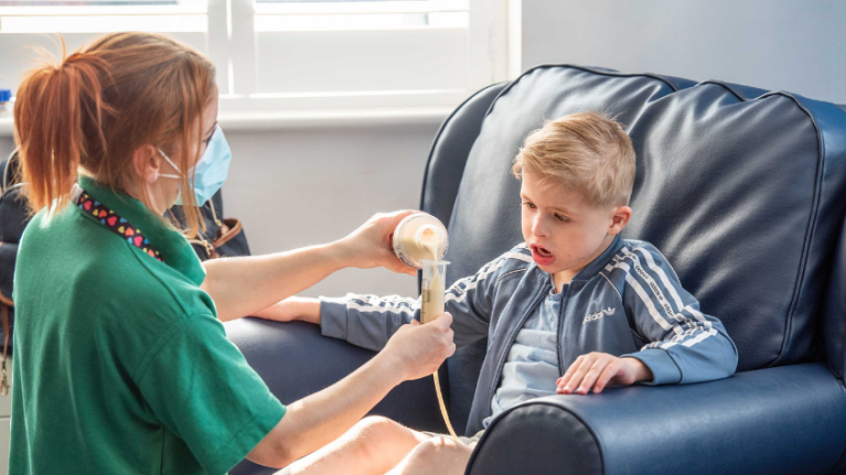 Nurse giving tube feed to young boy at a children's hospice