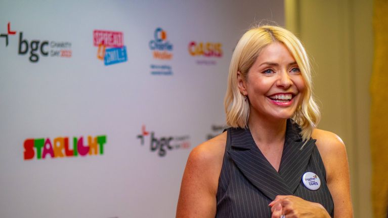 A woman in a black dress stands on the red carpet, smiling